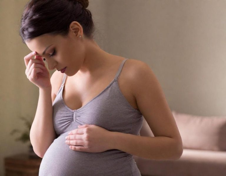 Schwangere Frau berührt ihren Bauch und wirkt emotional belastet